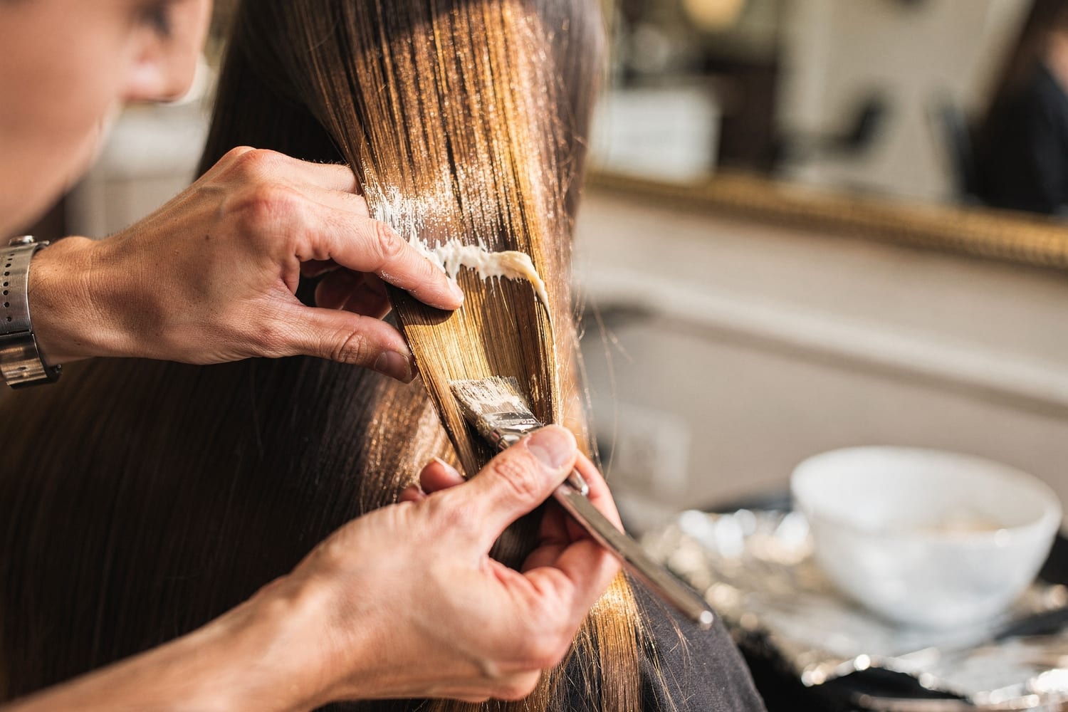 A stylist hand-painting balayage color onto a section of hair